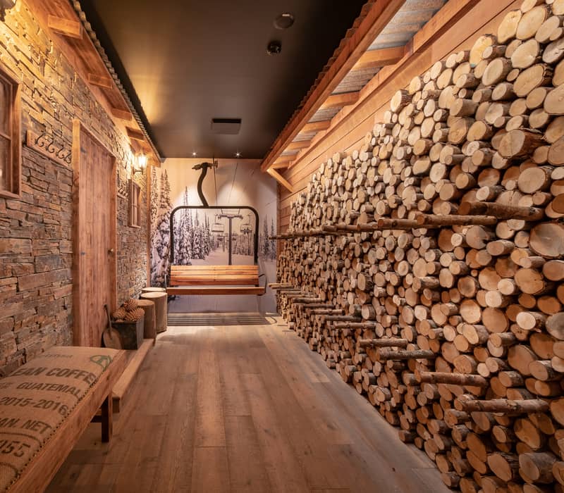 A rustic alpine hallway with stacked logs on one side and a schist stone wall on the other. Credit: Kamana Lakehouse